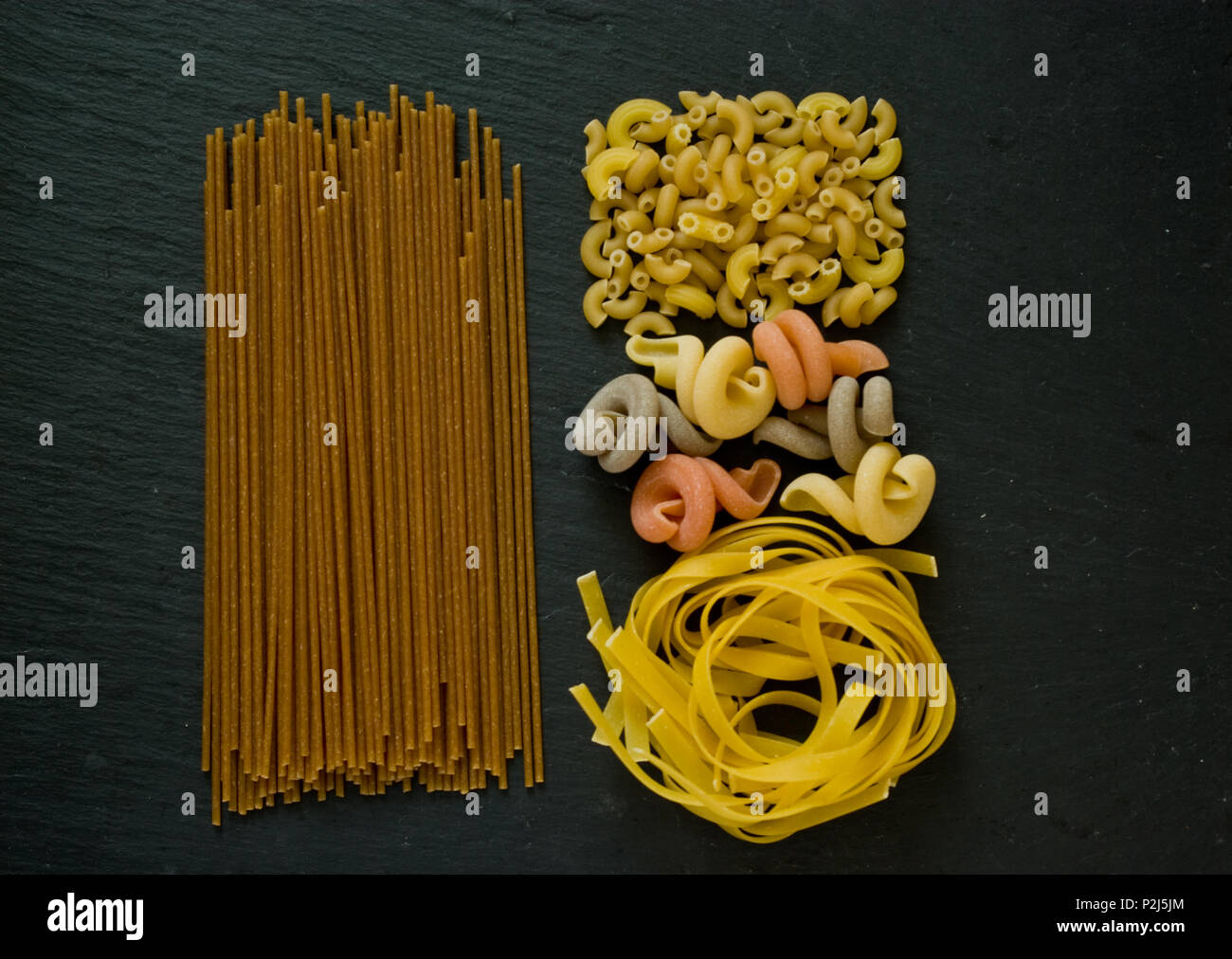 Assortimento di varietà italiane di pasta cruda laici piatta su una pietra nera con uno sfondo con spazio di copia Foto Stock