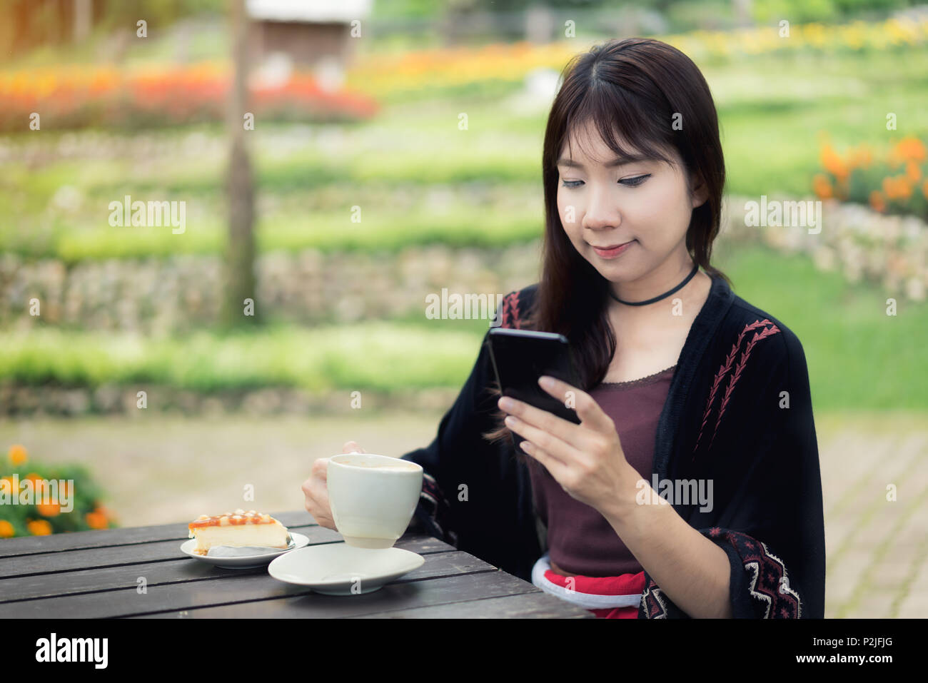 Belle Donne asiatiche hanno goduto nel giardino con caffè e chiacchierare in smartphone. Foto Stock