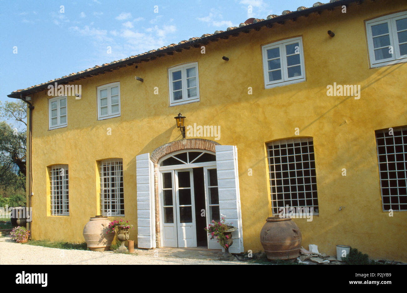 Esterno del dipinto di giallo villa toscana con persiane bianche su mezza doppia vetrata porte Foto Stock