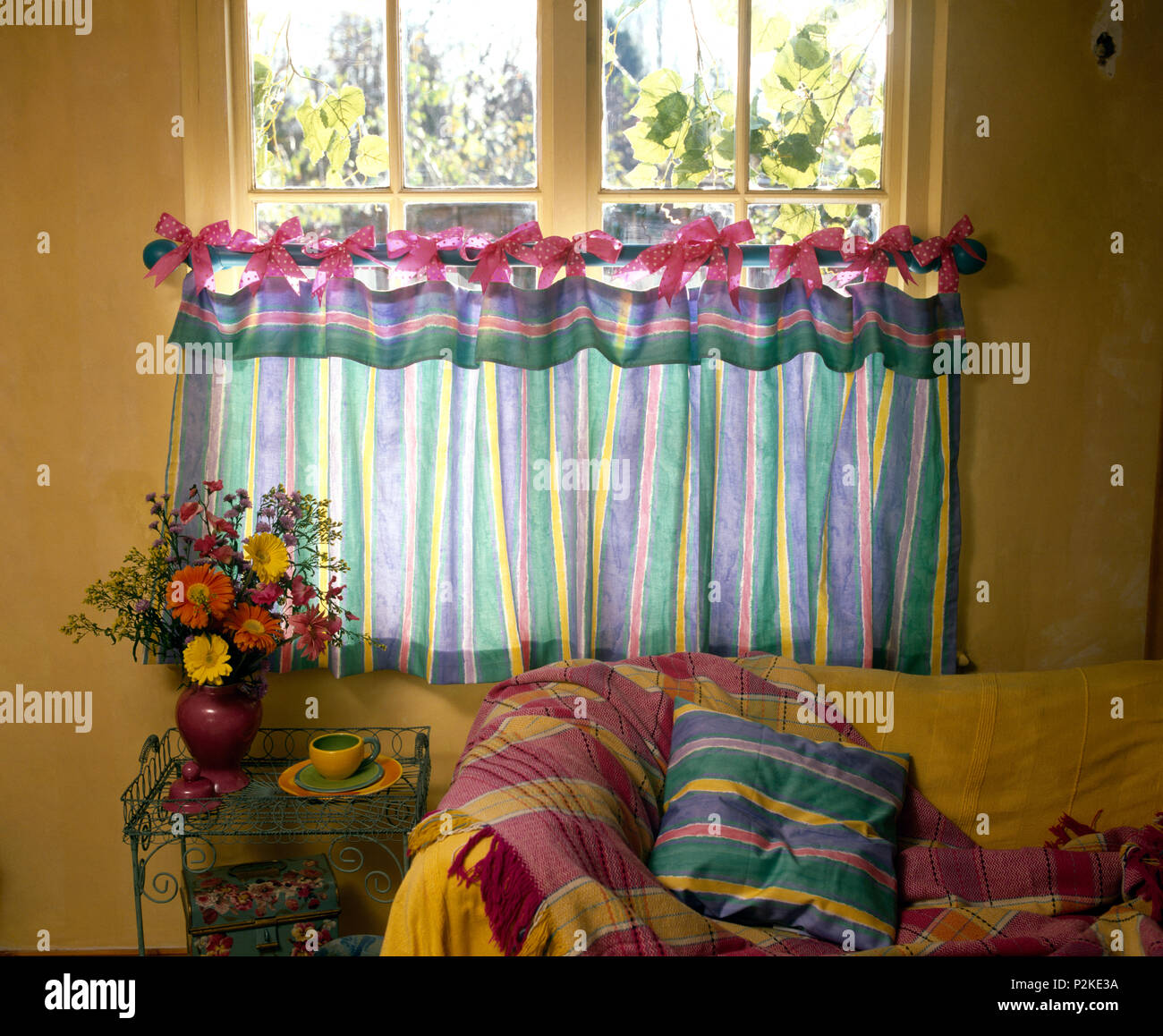 A strisce colorate cafe tende legati con archetti rosa su un'asta di ottone sul vetro in economia cottage in stile salotto Foto Stock
