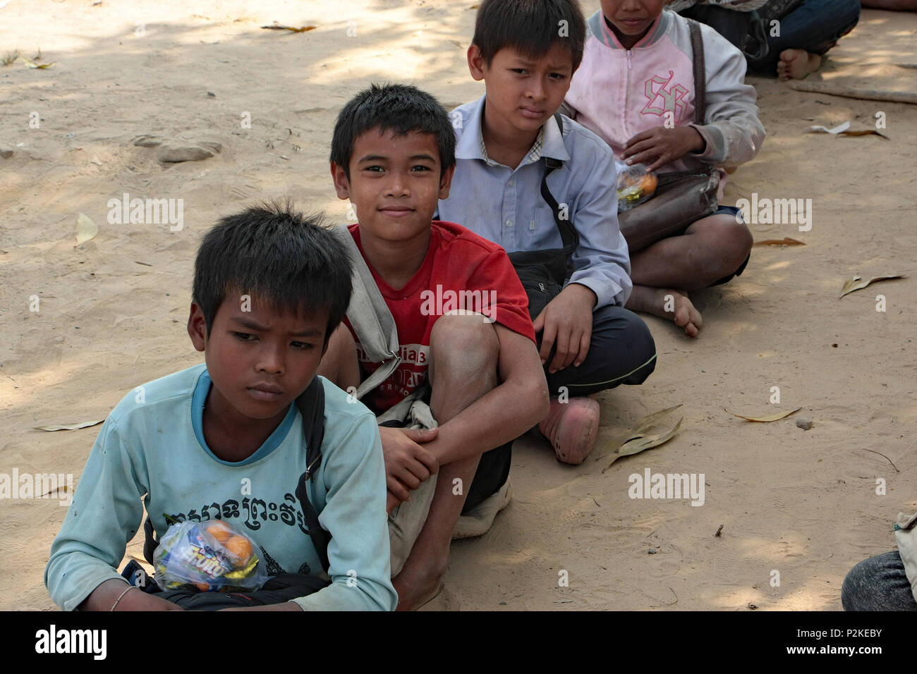 Scolari siedono in linea sul parco giochi in sabbia di risma scuola rurale in Cambogia. Foto Stock