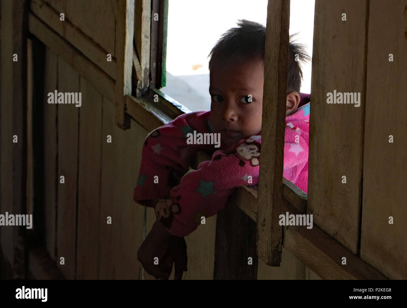 Una malinconica bambino guarda attraverso una finestra aperta in un'aula, rendendo il contatto visivo con la lente della fotocamera. Foto Stock