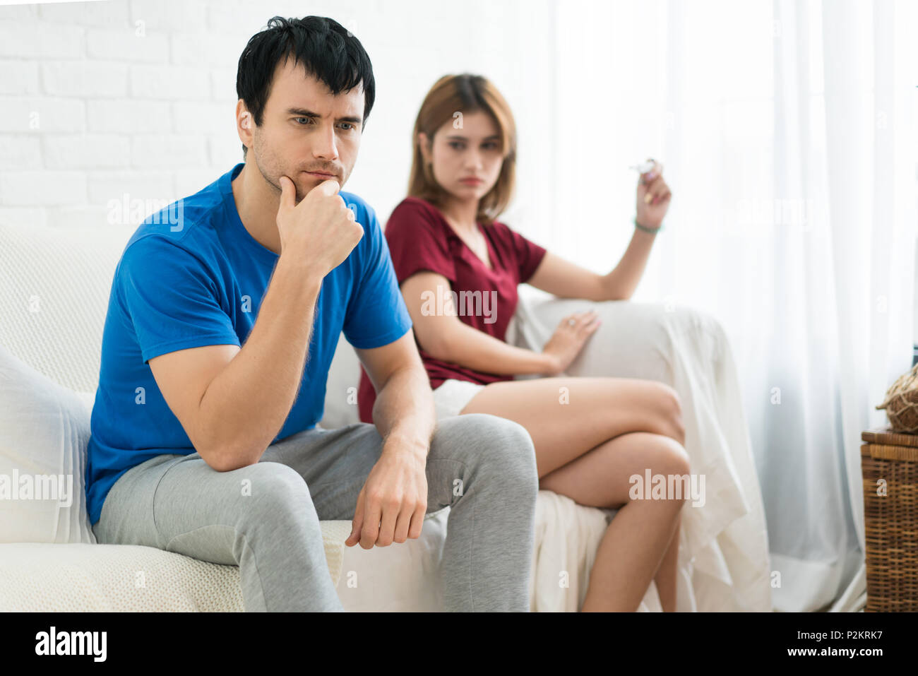 Frustrato marito uomo seduto accanto alla moglie cercando in test di gravidanza in mano moglie. Non è una buona notizia in mattinata Foto Stock