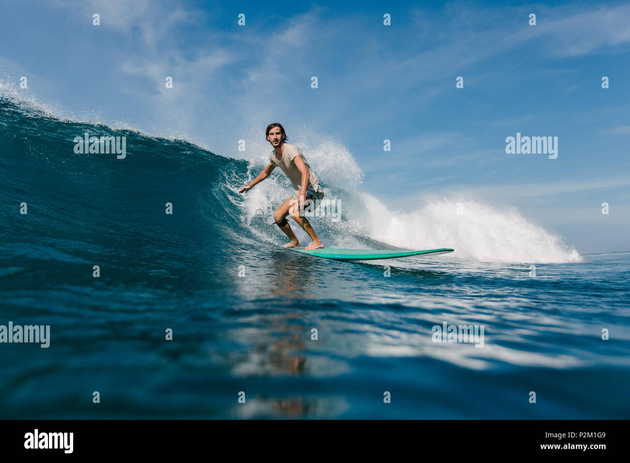 Barbuto giovane uomo in umido t-shirt cavalcando le onde sulla tavola da surf sulla giornata di sole Foto Stock
