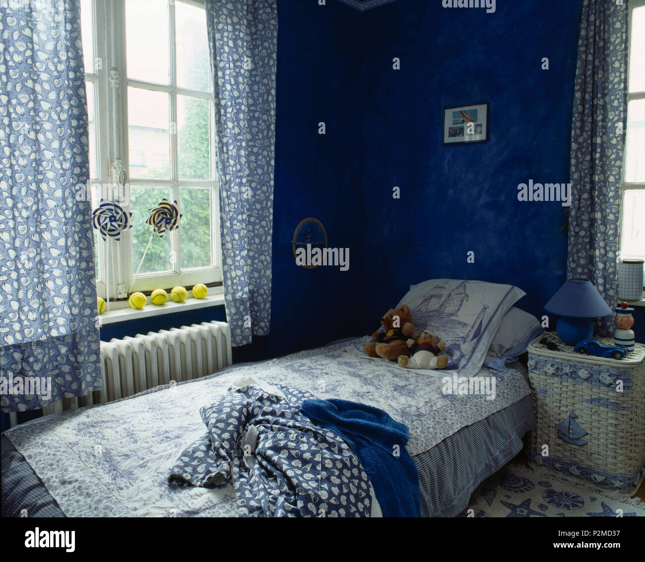 Blue+tende bianche sulla finestra al di sopra di un letto singolo con blue+trapunta bianca nel bambino camera blu Foto Stock