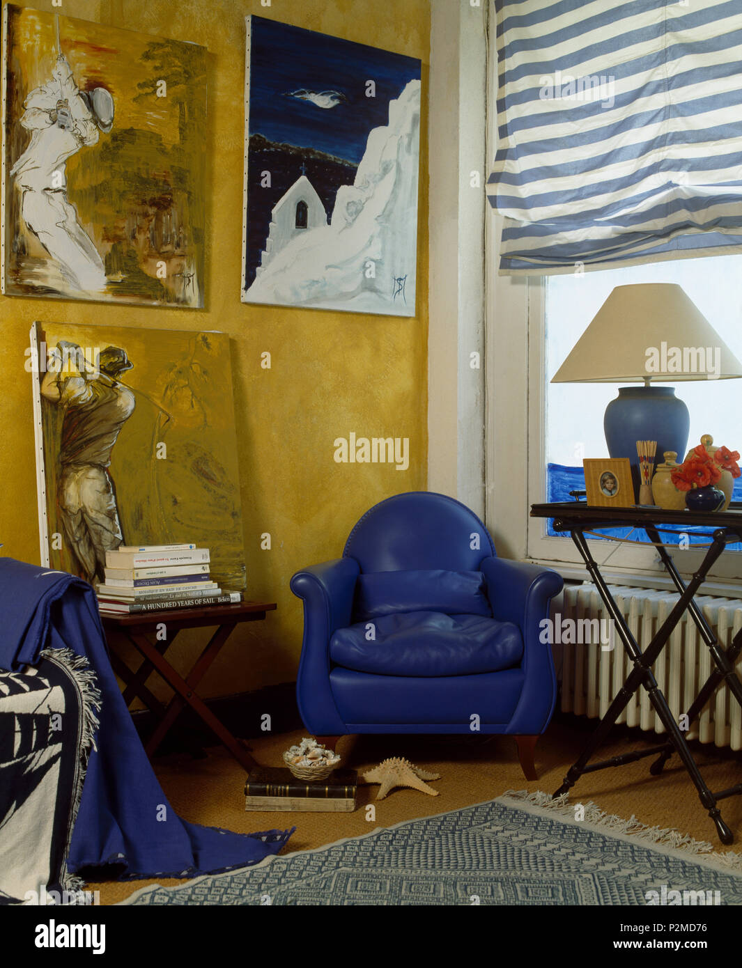 Grandi dipinti sulla parete al di sopra di un blu brillante poltrona in  pelle in un angolo del salotto con tenda a strisce sulla finestra Foto  stock - Alamy