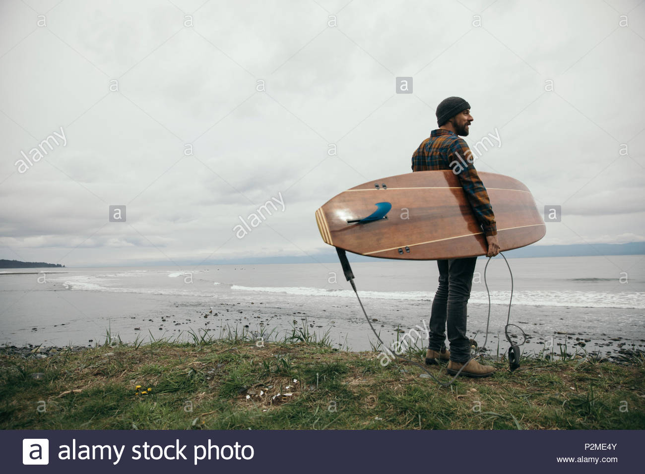 Surfista maschio con la tavola da surf a guardare oceano robusto in previsione Foto Stock