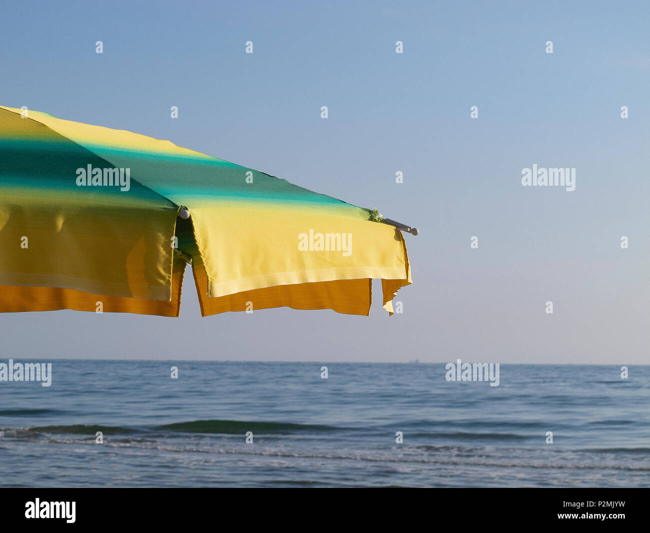Ombrellone giallo e verde, con lo sfondo del mare e cielo blu Foto Stock