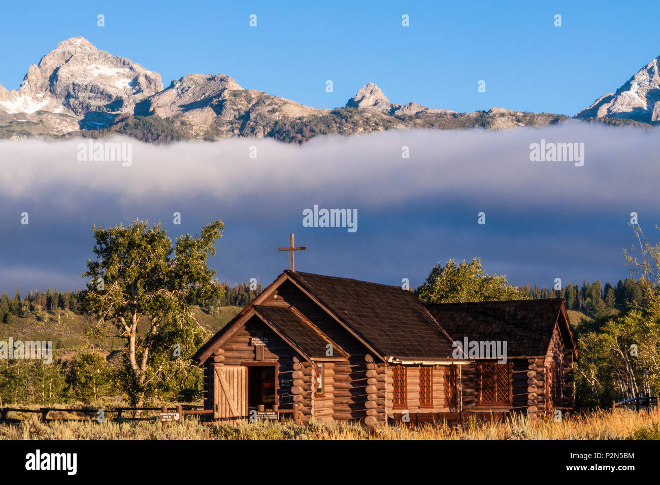 Grand Tetons Mountain Range e la Cappella vescovile della Trasfigurazione di sunrise, inondati di mattina presto la luce con la nebbia e nubi a bassa quota. Foto Stock