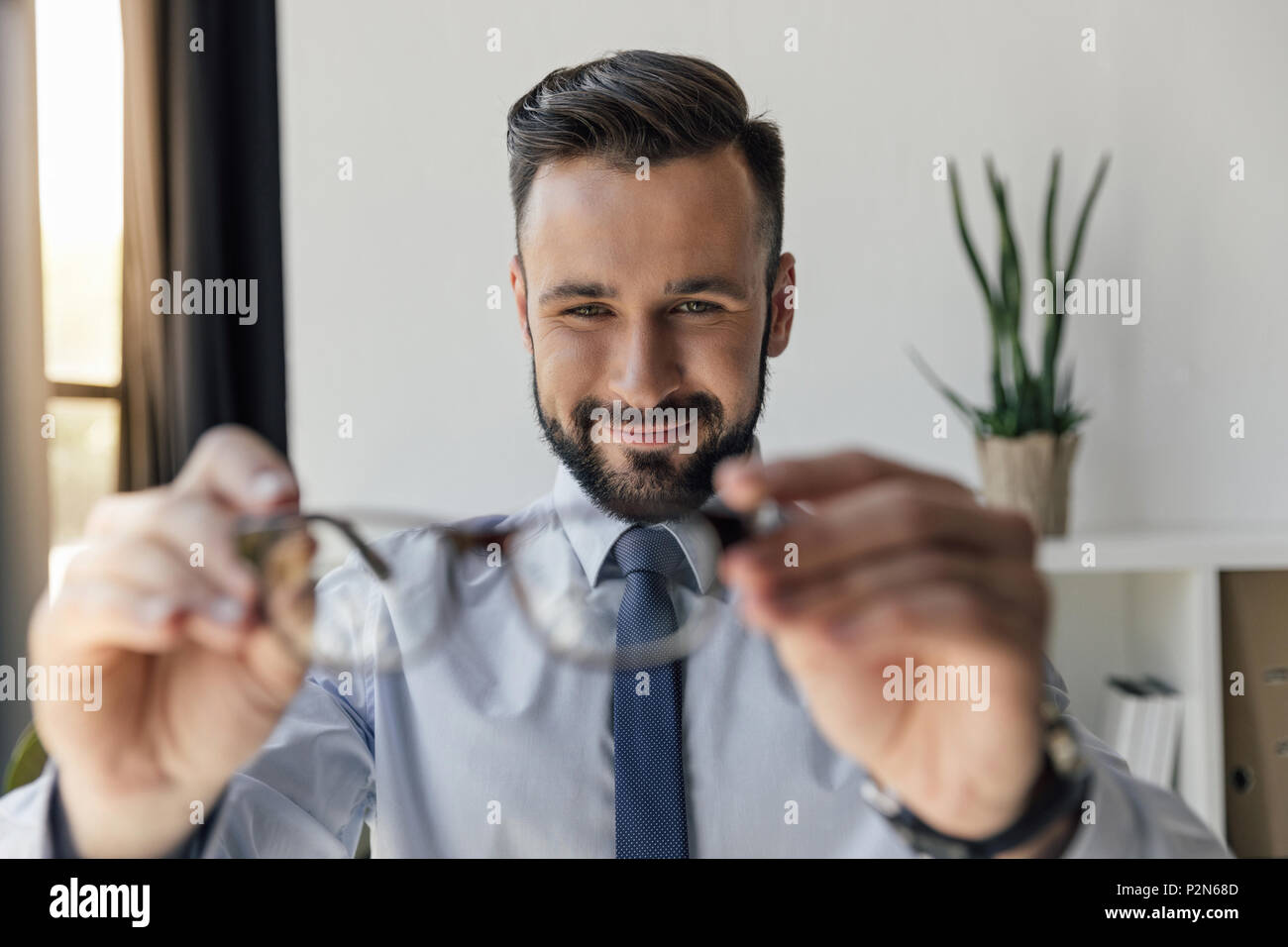 Messa a fuoco selettiva di imprenditore sorridente guardando un paio di occhiali in mani Foto Stock
