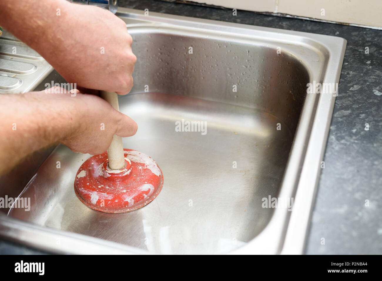 Uomo con uno stantuffo con due mani e acqua nel lavello, utilizzati per pulire un ostruito / bloccato lavello da cucina Foto Stock