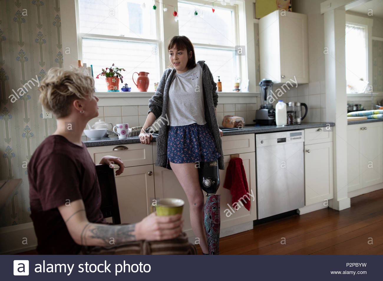 Giovane donna amputato di bere caffè, parlando con il mio ragazzo in cucina Foto Stock