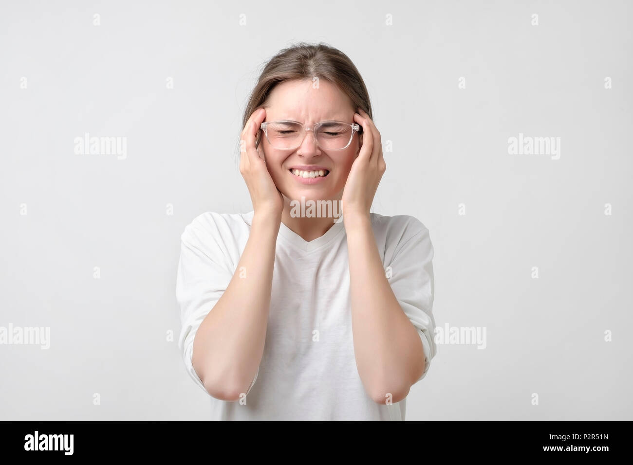 Ragazza europea in t-shirt bianco soffre di un terribile mal di testa e comprime la testa con le dita. Concetto di dimenticare e ricordare qualcosa, soffrono Foto Stock