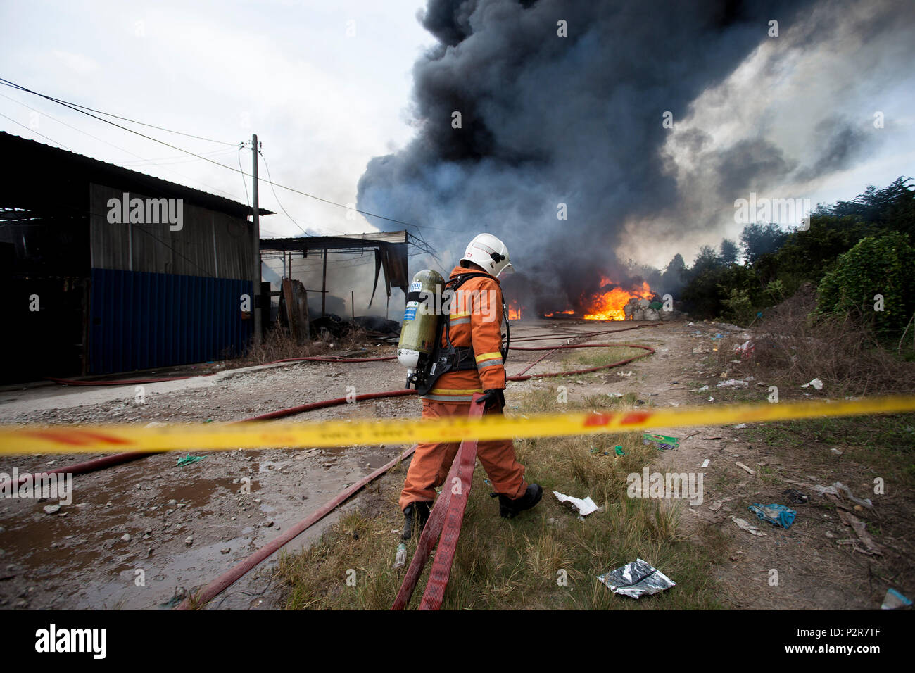 Un vigile del fuoco è tirando un modello Firehose verso una fabbrica di masterizzazione in Sungai Petani. Il fuoco si è rotto al 1:00 PM e rasa al suolo una plastica centro di riciclaggio, un compensato di elaborazione e di fabbrica un cofanetto fabbrica. Più di 20 camion fuoco sono state disperse per il controllo di un incendio di grandi dimensioni a causa di condizioni di vento e di prodotti infiammabili. Foto Stock