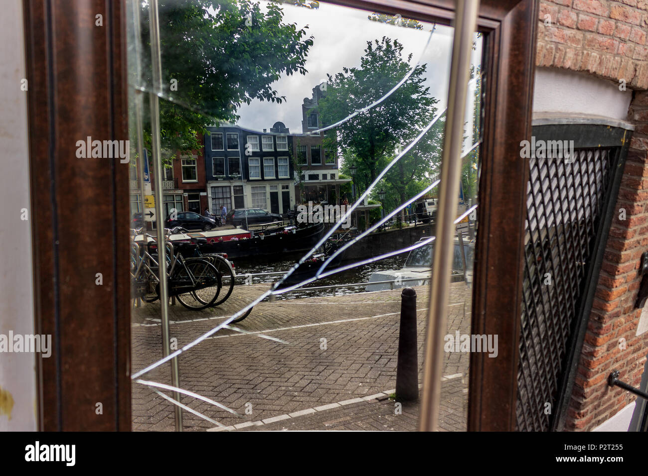 Un scartato specchio rotto riflette ancora un idilliaco paesaggio di una casa galleggiante, case e biciclette fodera un canale di Amsterdam, Paesi Bassi. Foto Stock
