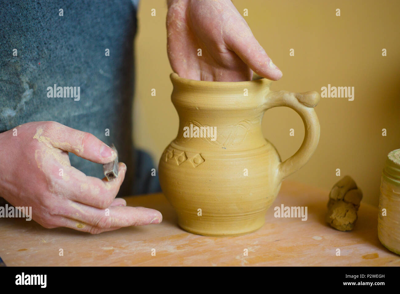 Professional potter rendendo pattern sul vaso di argilla con l'attrezzo speciale nel laboratorio di ceramica, studio. Creazione, artwork e concetto di fatti a mano Foto Stock