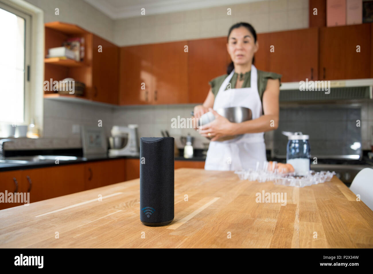 Donna nella sua cucina guardando il suo smart speaker Foto Stock