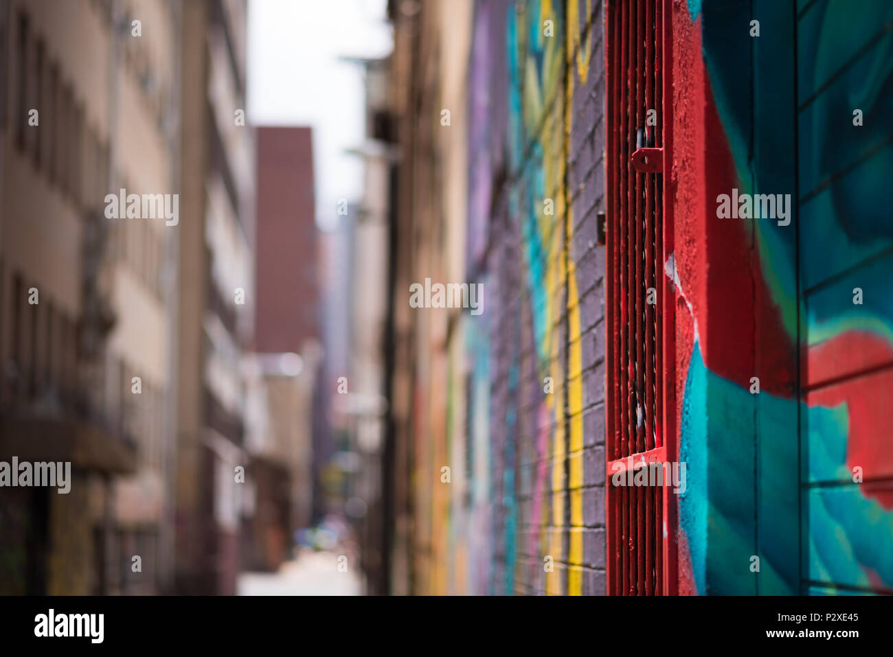 Una vista astratta di una città interna allyway a Johannesburg, luminosamente decorate con colorati graffiti, focalizzata sul primo piano e sfocata in d Foto Stock