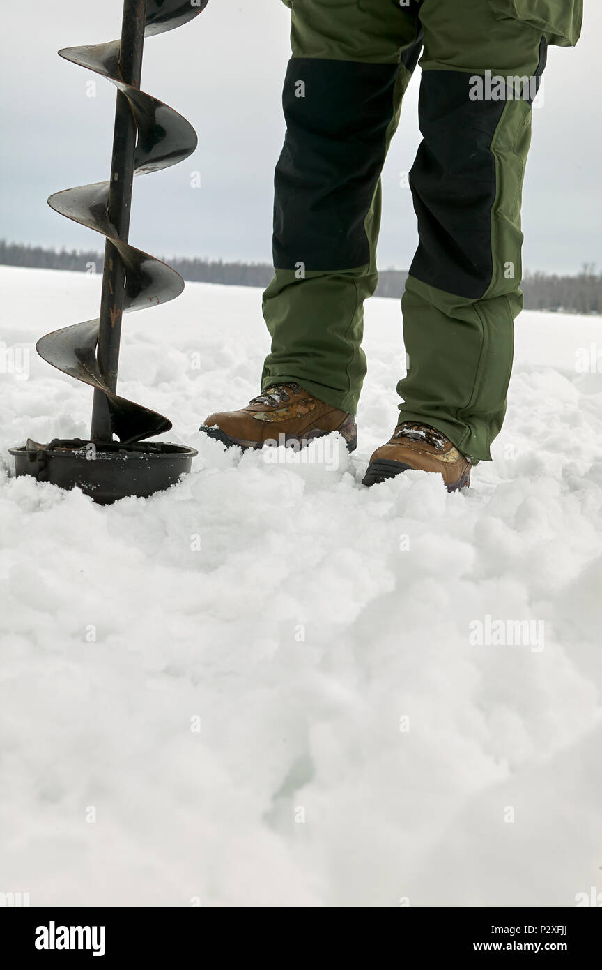 Man foro di perforazione in ghiaccio con grandi seminatrice sul giorno di inverno Foto Stock