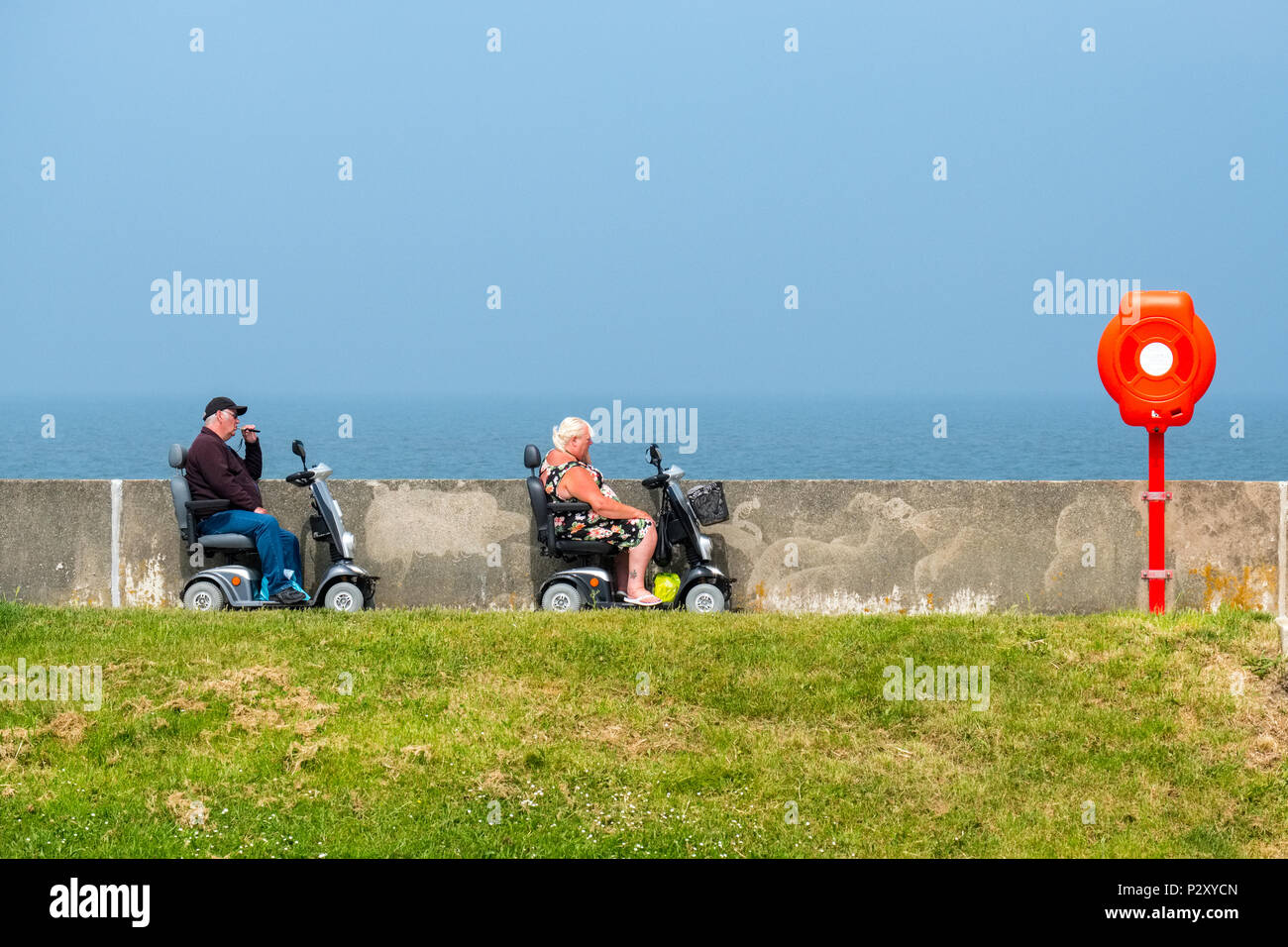 Due persone in mobilità scooter su una passeggiata sulla costa settentrionale del Galles Foto Stock