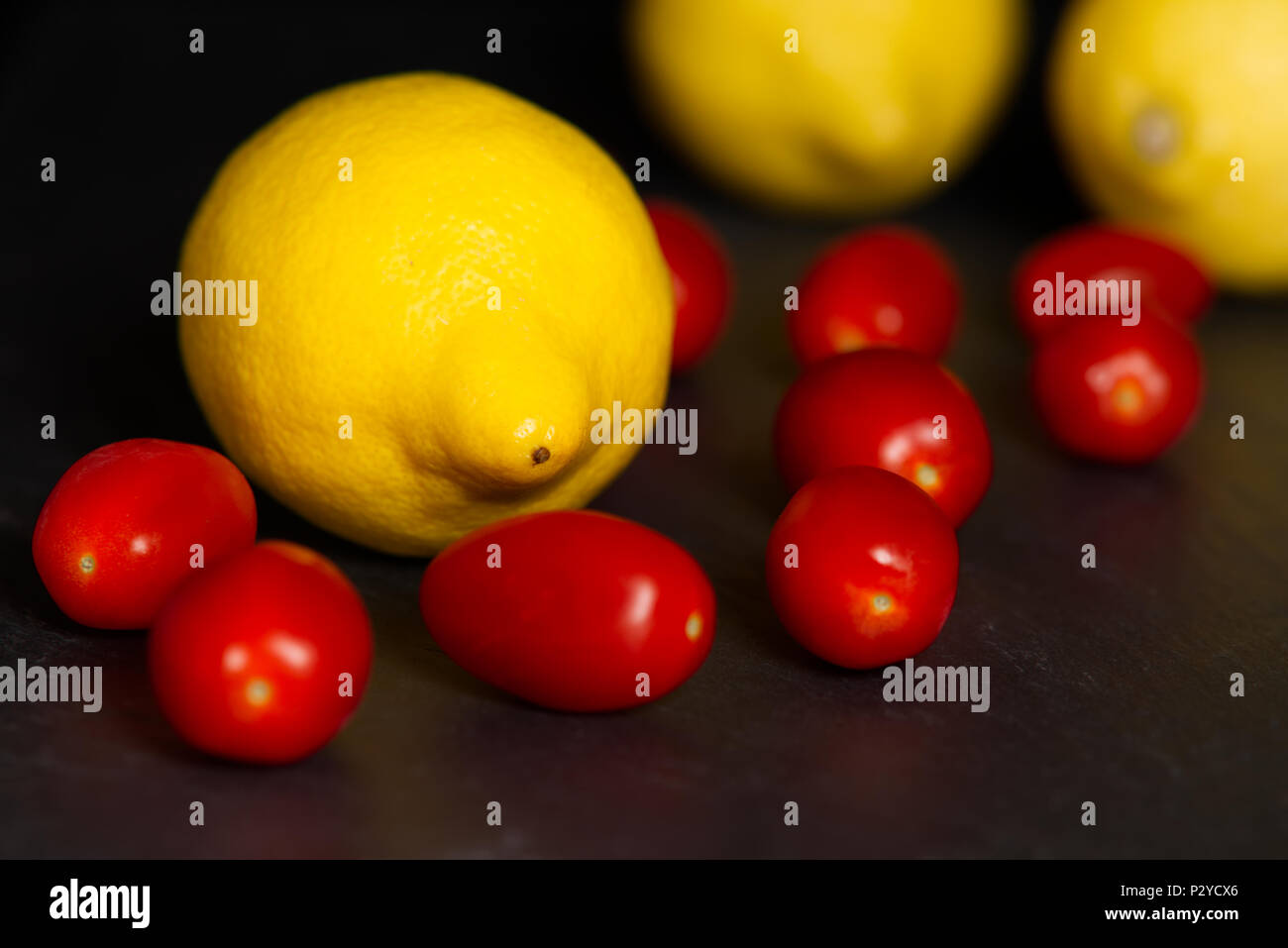 Limoni giallo e rosso baby i pomodorini isolata su uno sfondo scuro su un superficie di ardesia. Frutta mangiare sano concetto Foto Stock