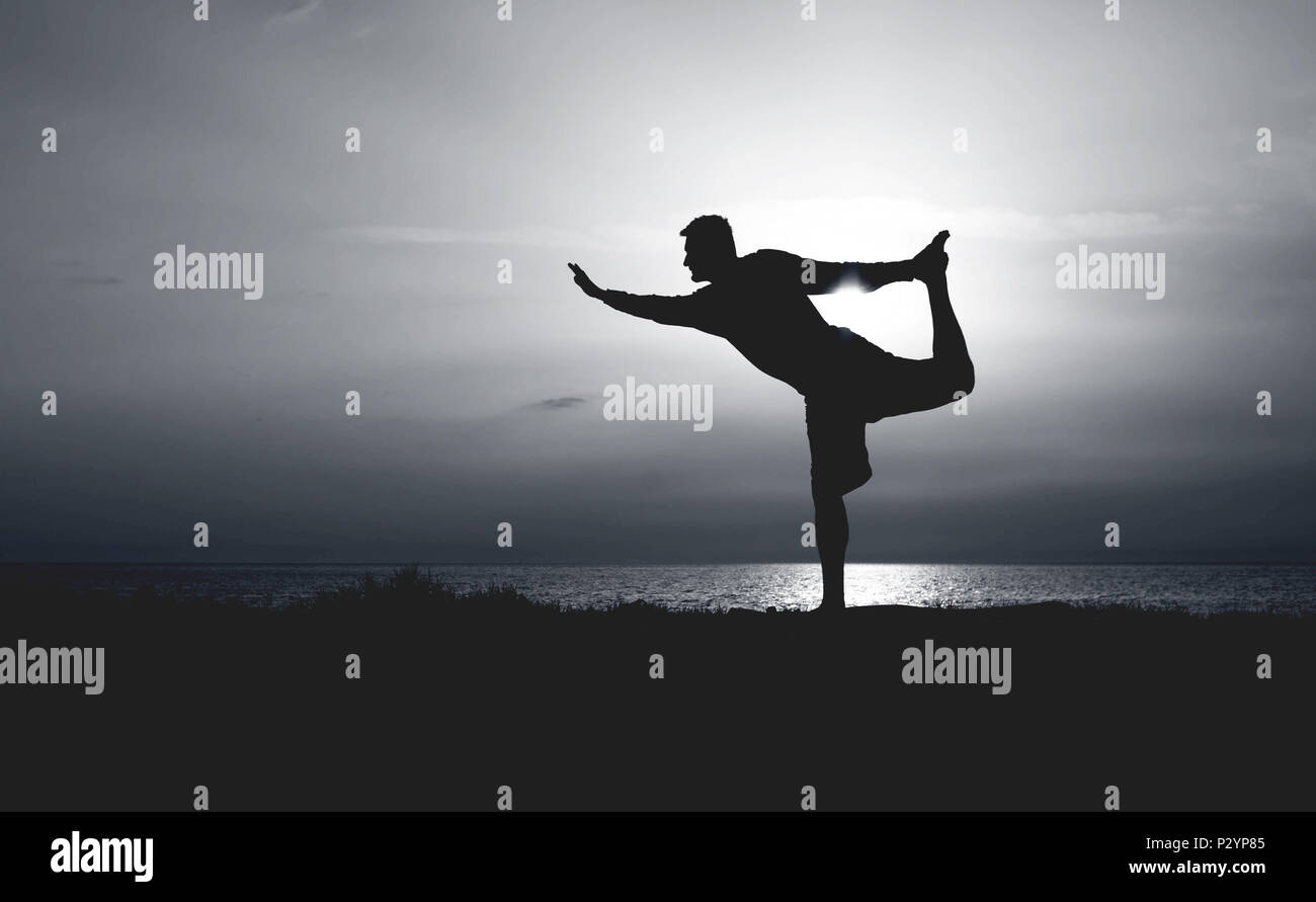 Silhouette di un giovane uomo la pratica dello yoga. Tramonto sul mare. Centina permanente di porre o Dandayamana Dhanurasana. Foto Stock