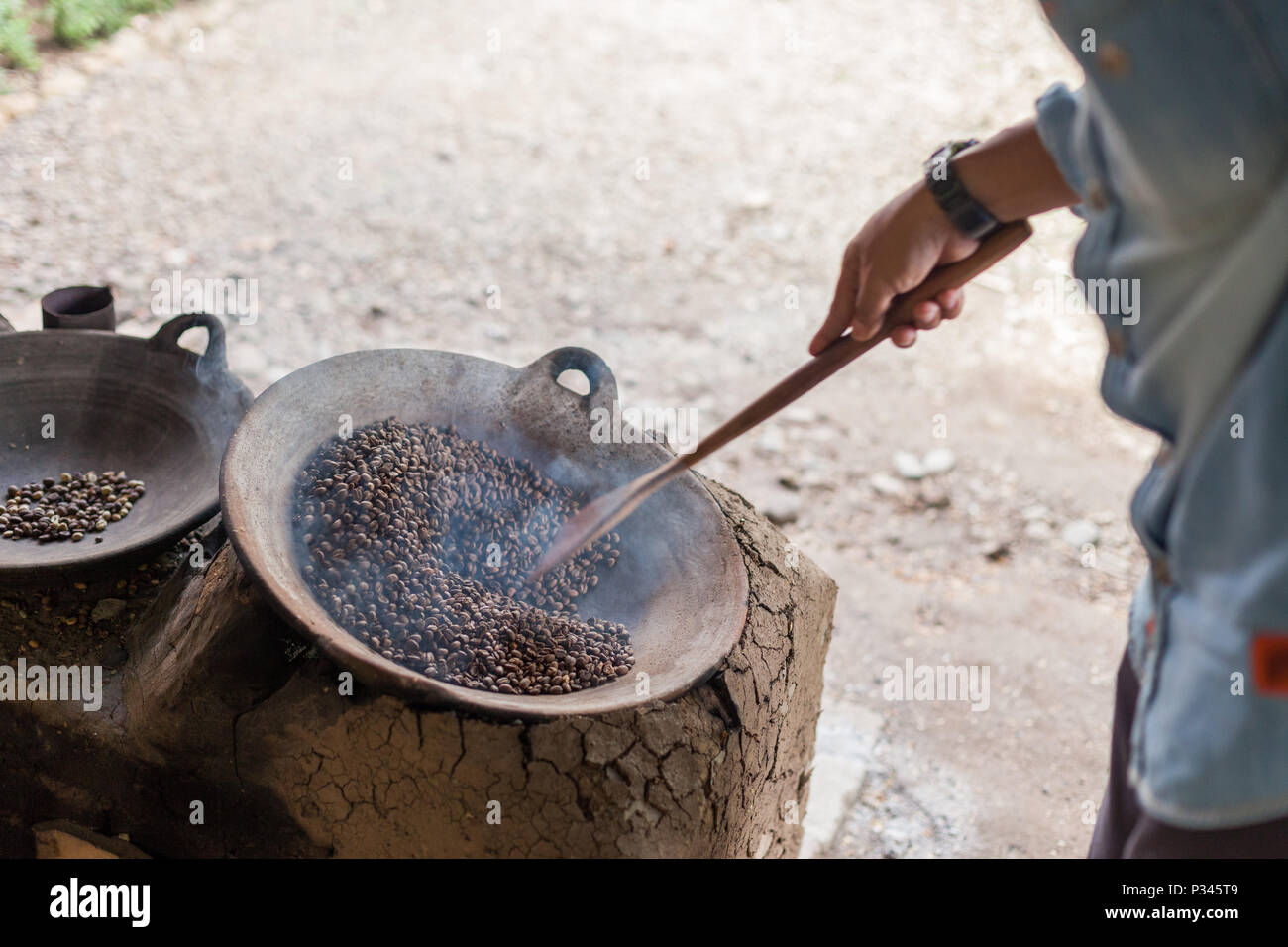 Master girarrosti arrosto manualmente i chicchi di caffè in un legno-sparò stufa vicino Banyuwangi, Java, Indonesia Foto Stock