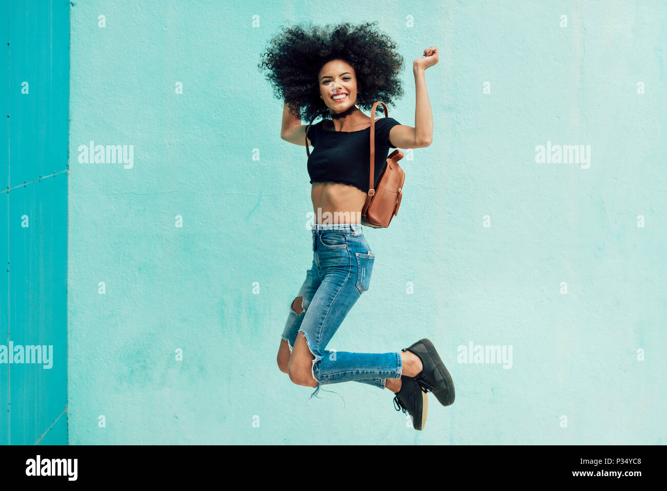 Giovane donna misti con capelli afro jumping all'esterno. Femmina di indossare abiti casual in background urbano. Il concetto di stile di vita Foto Stock