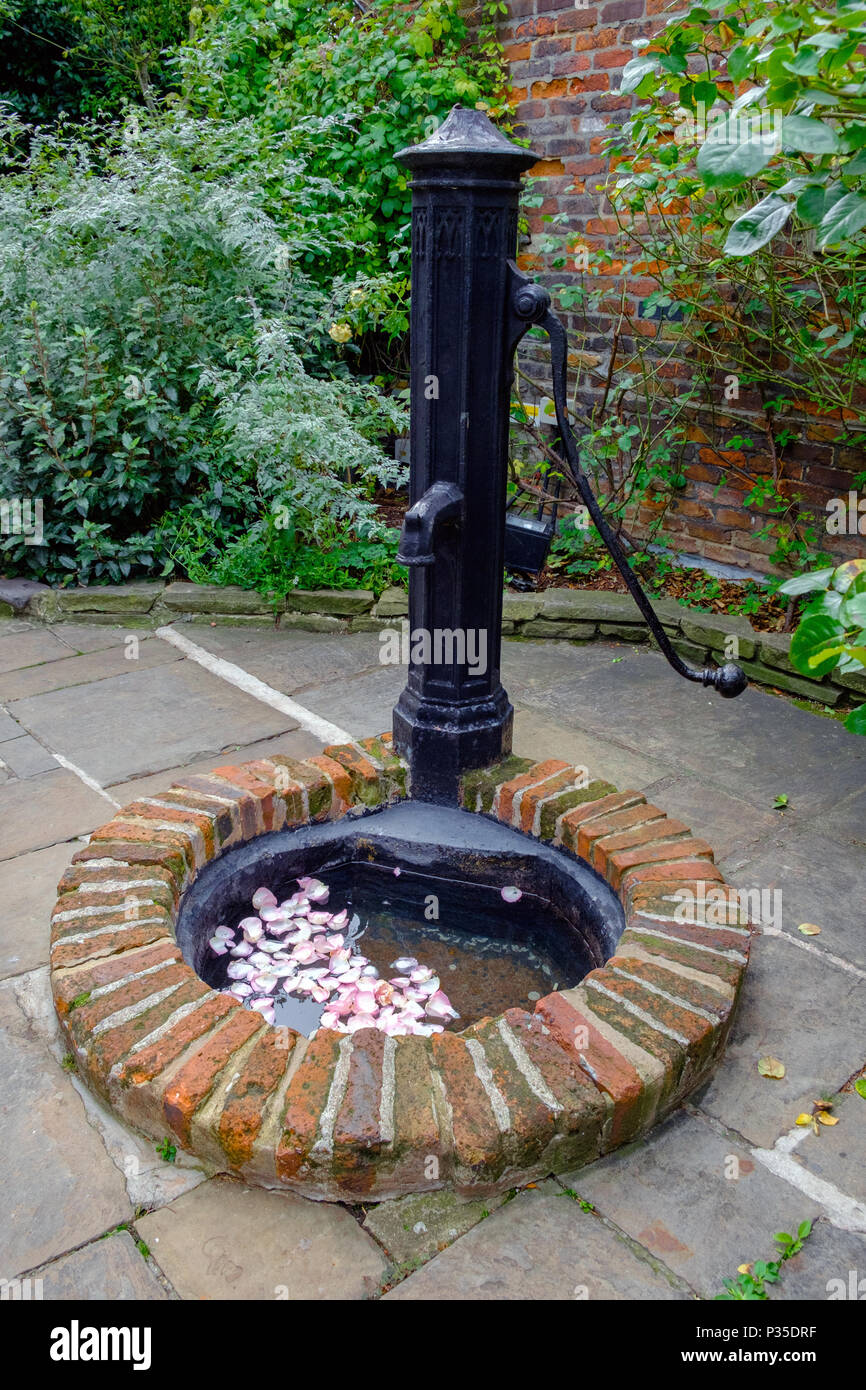 Ghisa giardino pompa acqua al tetto di Kensington Gardens Situato al di sopra di Kensington High Street. Petali di fiori in acqua. Cespugli di verde e un muro di mattoni. Foto Stock