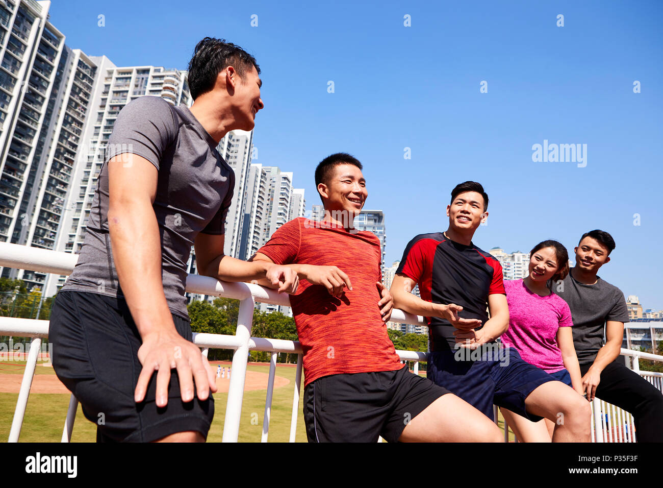 Un gruppo di giovani asiatici adulti parlare in chat rilassante in uno stadio durante il riposo durante l'esercizio Foto Stock