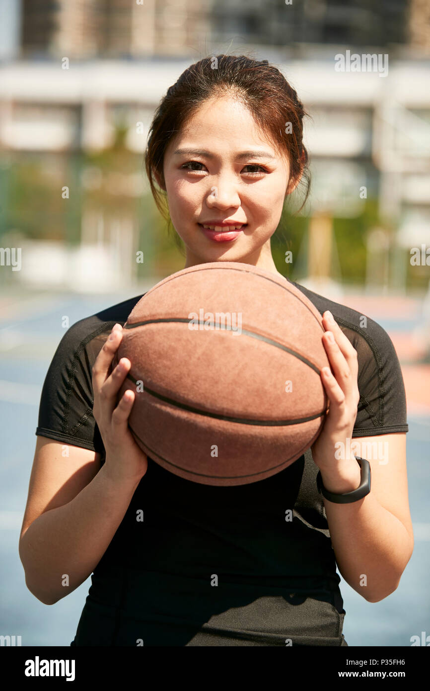 Giovane donna asiatica in possesso di un basket guardando la telecamera sorridendo. Foto Stock