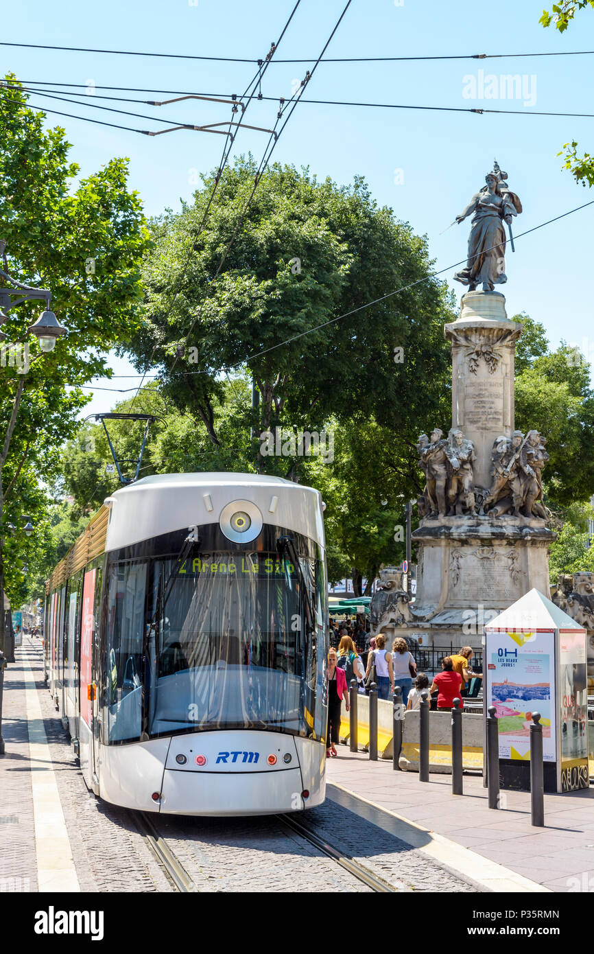 Un T2 tramvia la guida verso il basso da Canebiere e passando per il monumento al 1870 guerra morti situato in Leon Blum park, con la gente che camminava lungo il Foto Stock