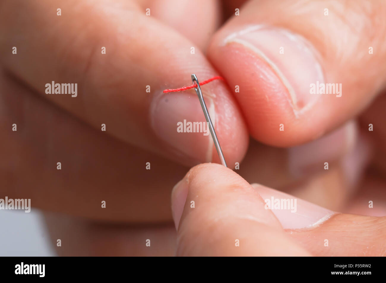 Vicino la mano che regge il rosso filettato con aghi di cucitura. Selezionare la messa a fuoco leggera profondità di campo e sfondo sfocato. Foto Stock