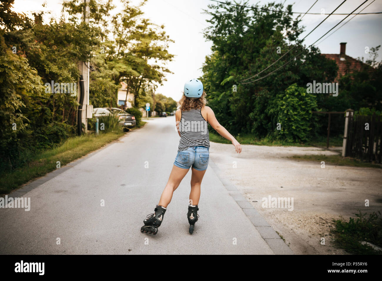 Donna pattinaggio su strada di città con il casco in estate da dietro Foto Stock
