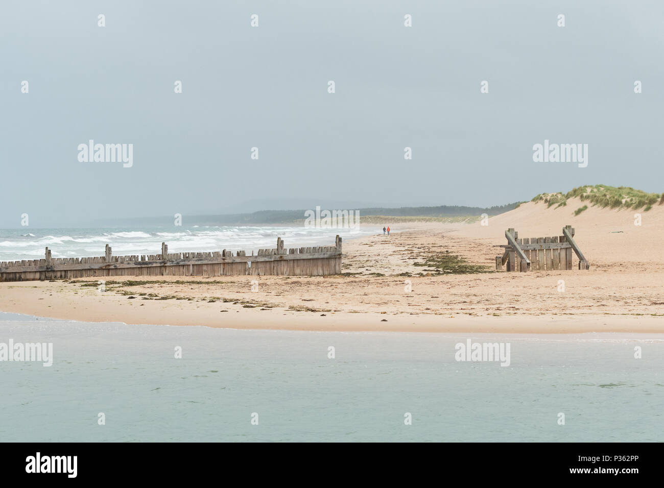 Lossiemouth - giovane in distanza a piedi lungo Lossiemouth Spiaggia a Est verso pennelli di legno e il fiume Lossie, murene, Scotland, Regno Unito Foto Stock