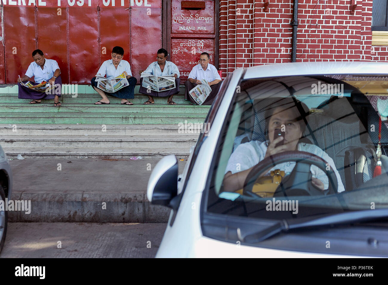 Yangon, Myanmar, uomini di sedersi di fronte il principale ufficio postale e leggere il giornale Foto Stock