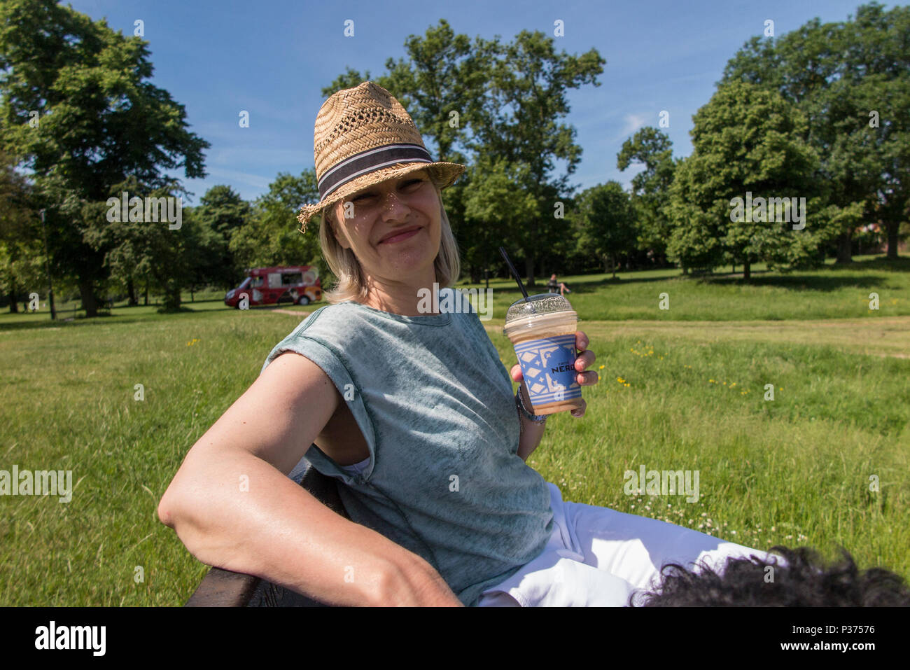 Una donna in un cappello di paglia gode di un caffè freddo in estate in un parco di Londra Foto Stock