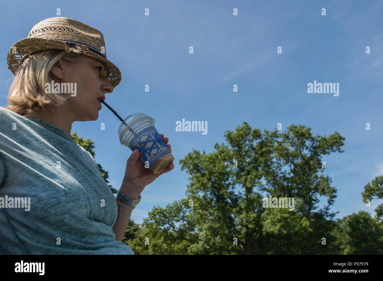 Una donna in un cappello di paglia gode di un caffè freddo in estate in un parco di Londra Foto Stock