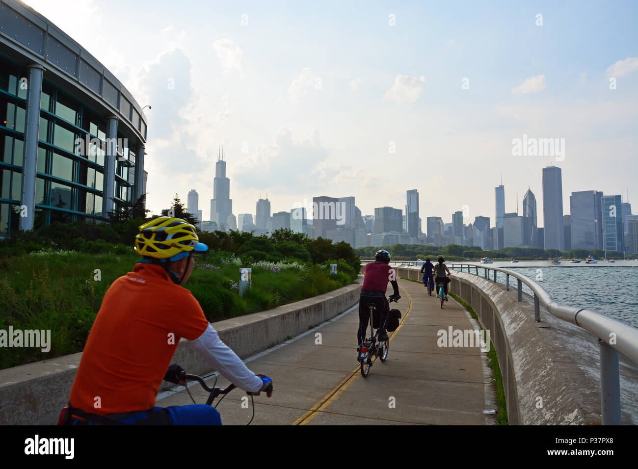 Chicago's skyline appare come ciclisti ride il lago pista ciclabile sul lato posteriore del Shedd Aquarium sul Lago Michigan e il Museo del Campus Foto Stock