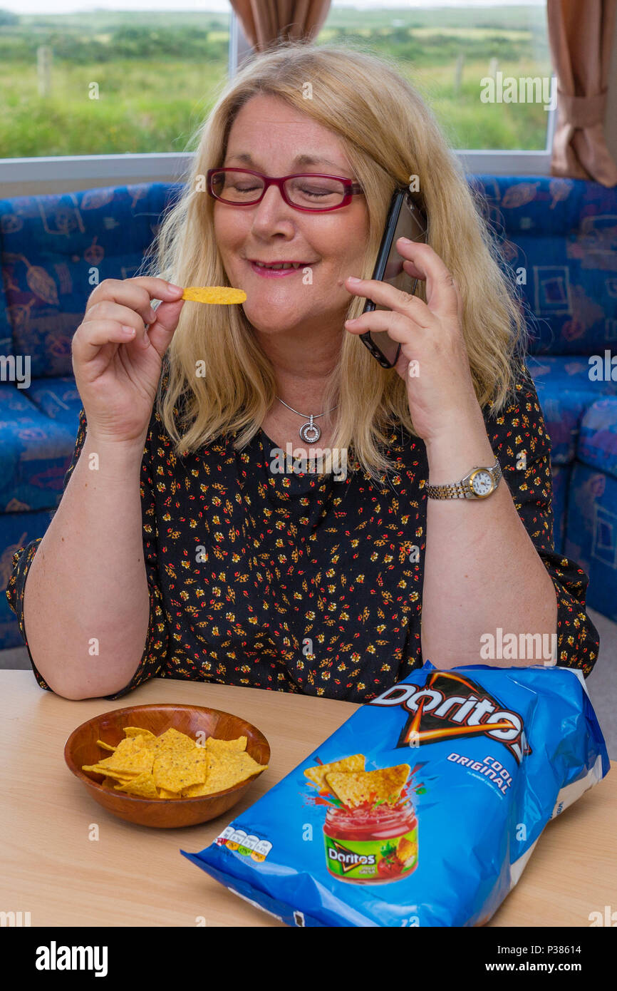 Donna bionda mangiare Doritos da una dimensione di condivisione di borsa e un piccolo recipiente Foto Stock