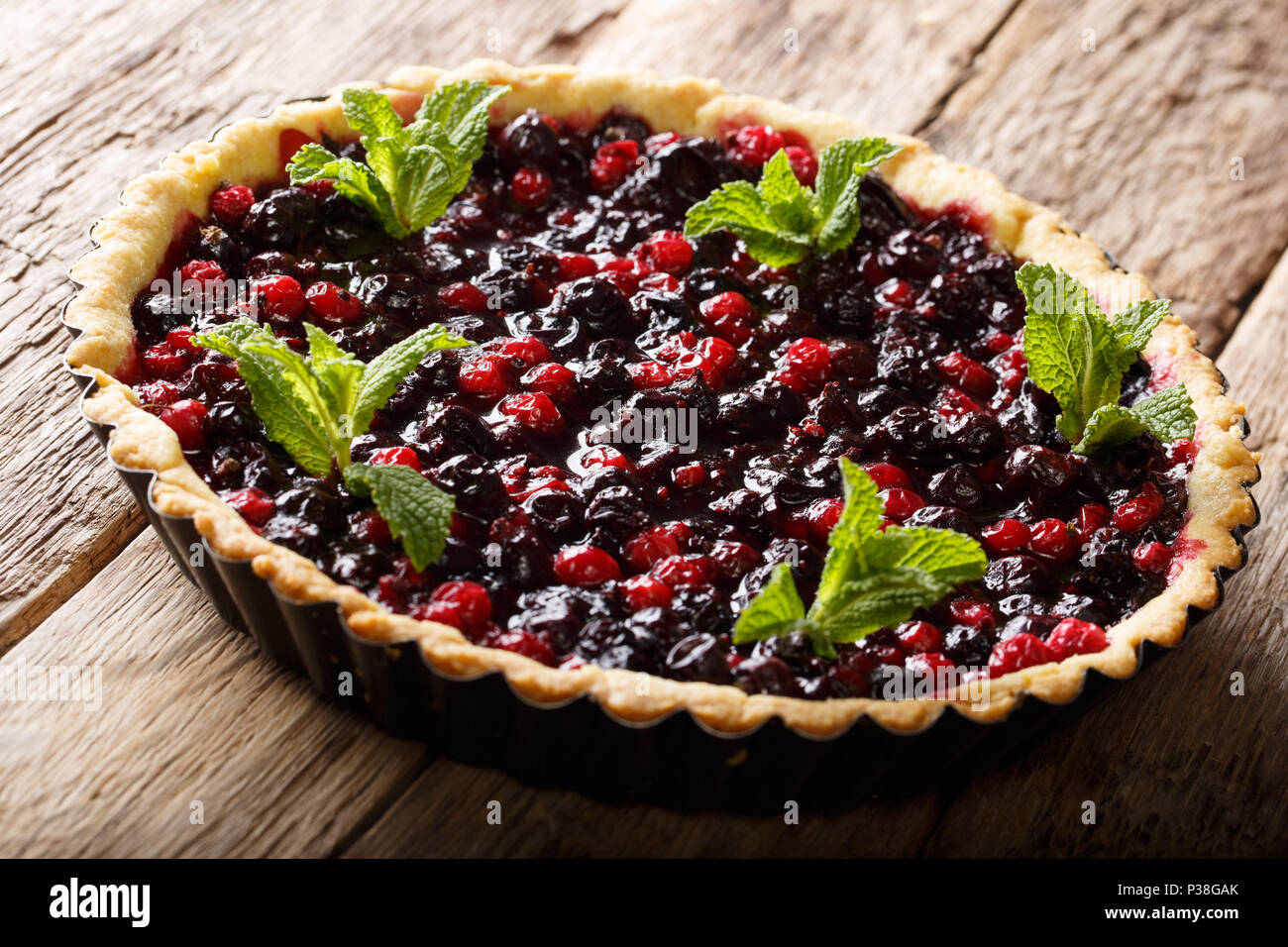 Rustico succosa crostata con bacche di ribes, mirtilli e mirtilli rossi close-up in una teglia su una tavola orizzontale. Foto Stock