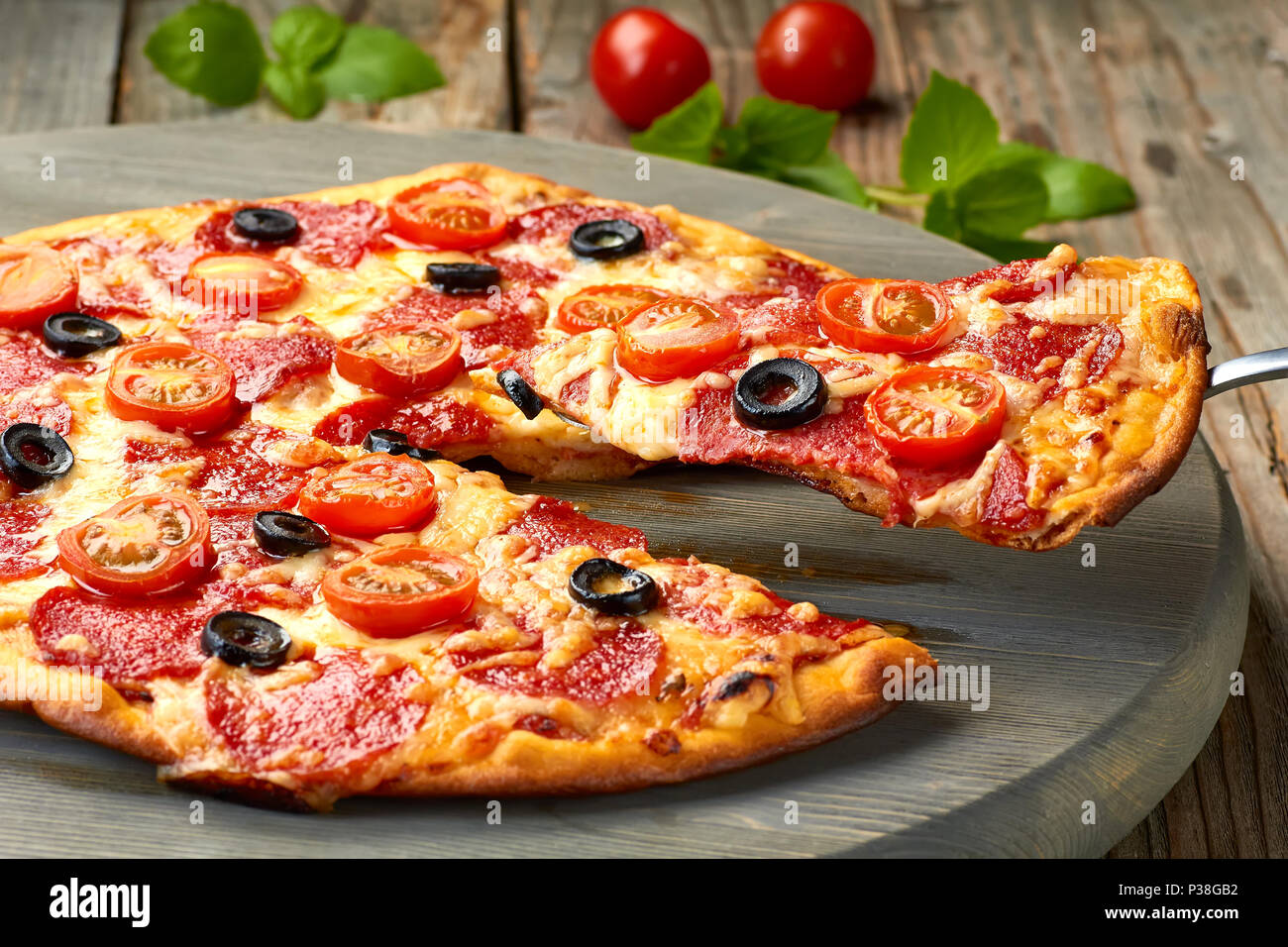 Sollevare fetta di salsiccia per pizza pizza con pomodori ciliegie e olive Foto Stock