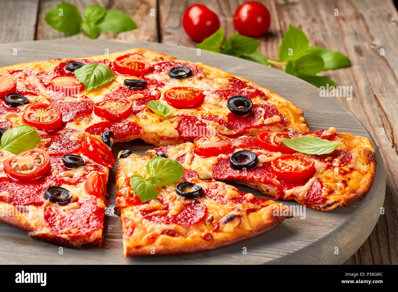 Salsiccia per pizza pizza con pomodori ciliegie di olive su un tavolo di legno Foto Stock