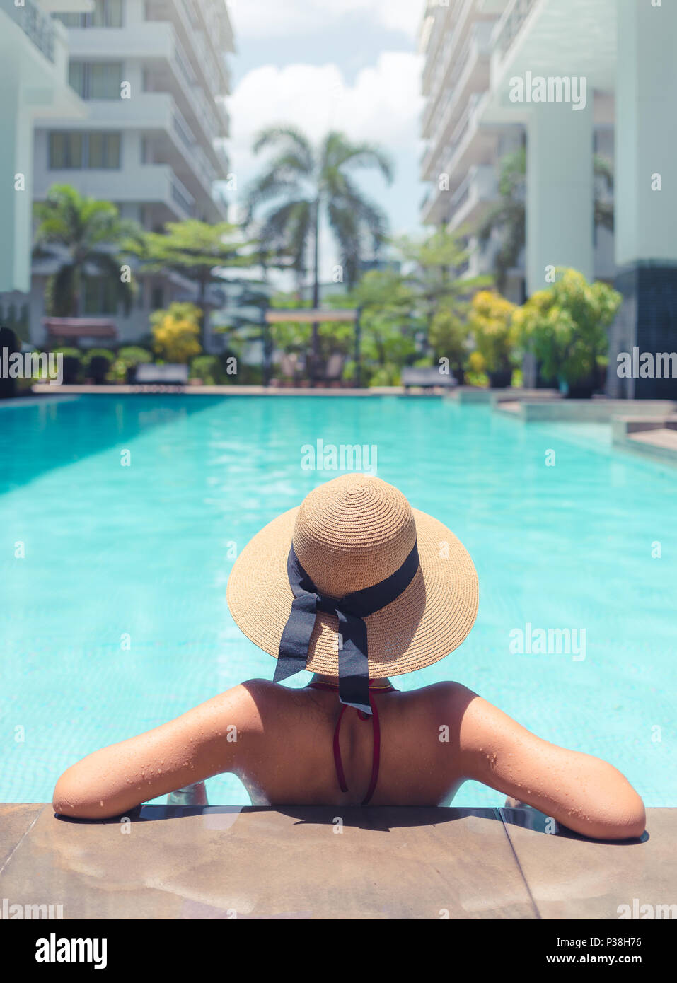 Donna con cappello marrone rilassante in piscina con acqua blu durante una giornata di sole , il concetto di vacanza Foto Stock