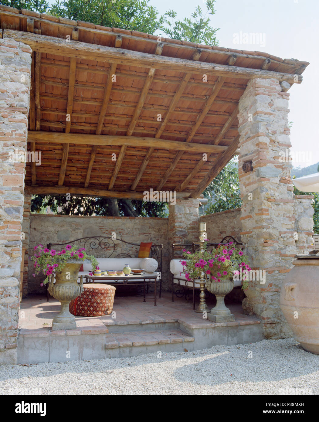 Ferro battuto divani con cuscini bianchi sulla veranda con piastrelle di terracotta e travi rustiche padiglione nel giardino della villa in Toscana Foto Stock