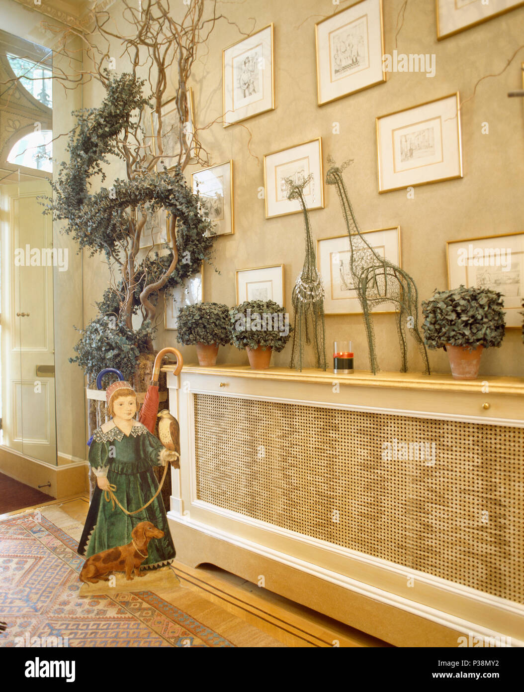 Una dimensionale figura in legno accanto a ramoscelli con fodera greenfoliage garland nella hall con il coperchio sul radiatore Foto Stock