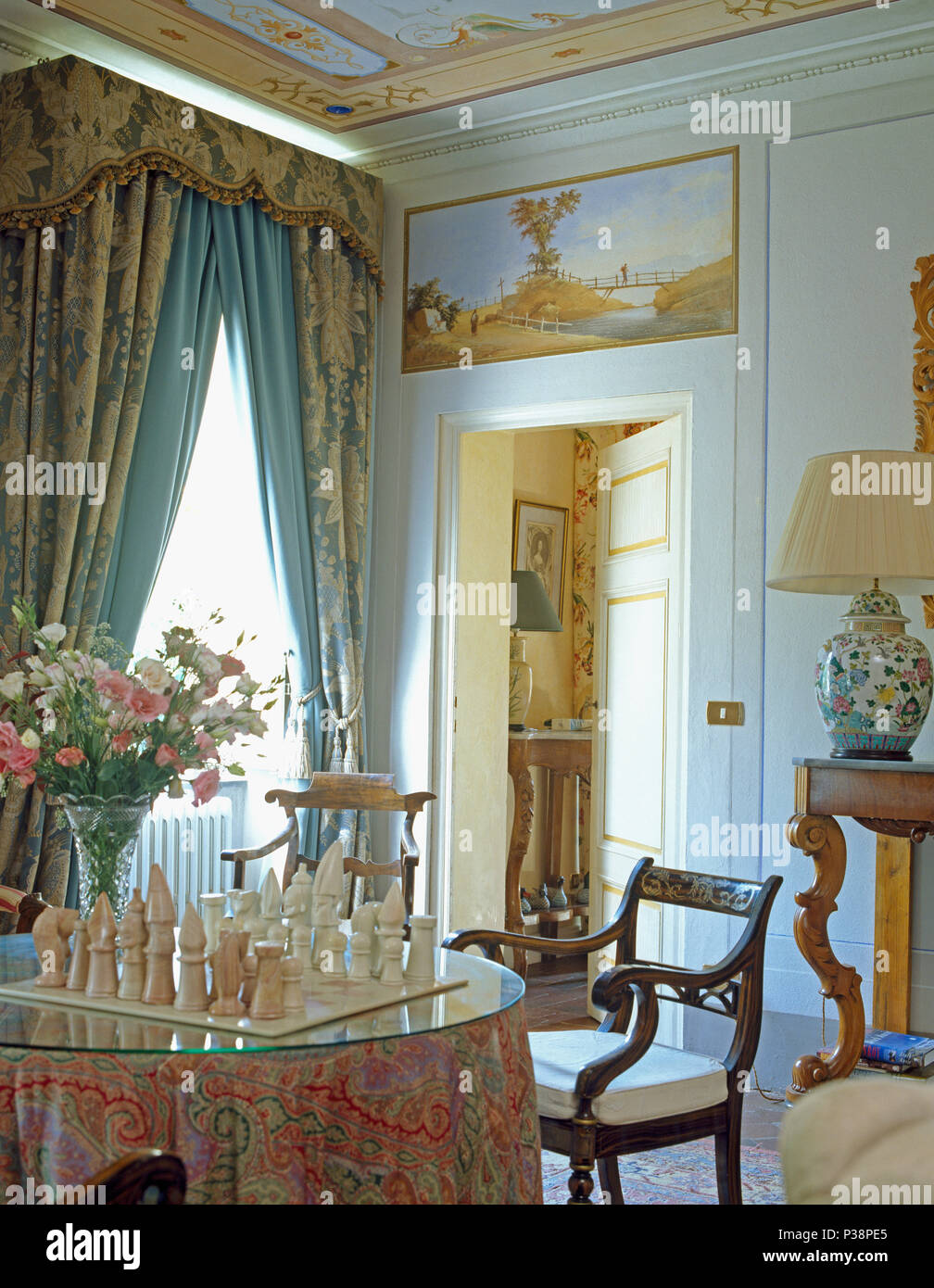 Set di scacchi sul tavolo da pranzo con panno modellato in Toscana elegante sala da pranzo con pesanti blu e tende color crema Foto Stock