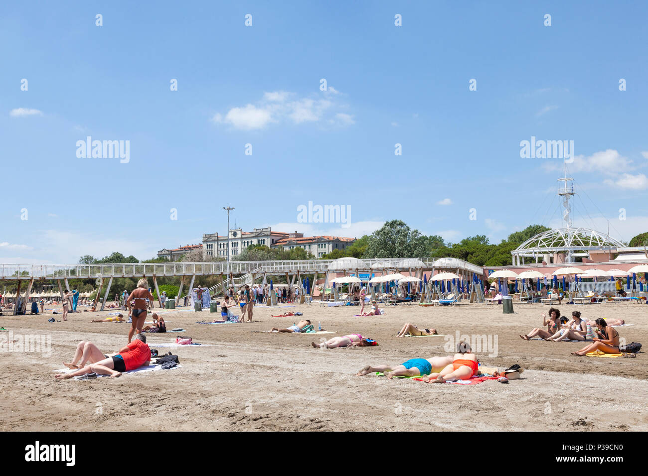 La gente a prendere il sole sulla sabbia di fronte al molo e il ristorante Blue Moon Beach, Lido di Venezia, l'isola del Lido di Venezia in tarda primavera Foto Stock