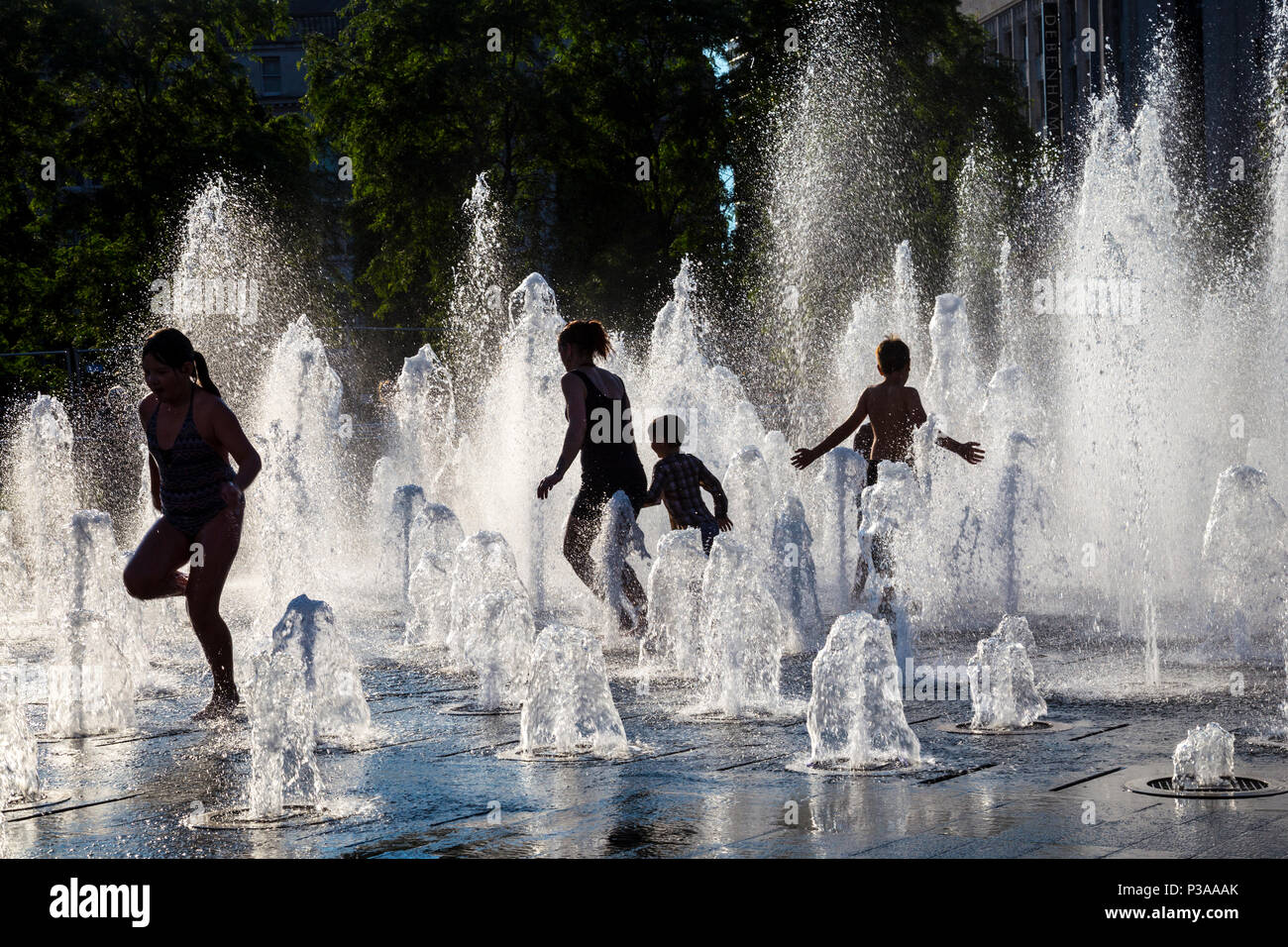 Sagome di bambini che corrono attraverso una fontana in estate, Piccadilly Gardens, Manchester, Regno Unito Foto Stock