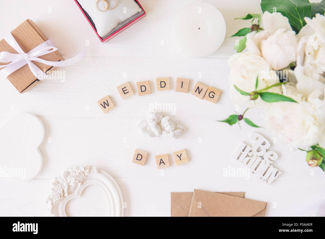 Layout con un giorno di nozze scritto in blocchi di legno, statuetta di due splendidi angeli, giftbox, anelli, cartoline, cuore telaio sagomato e peonie bianco su t Foto Stock